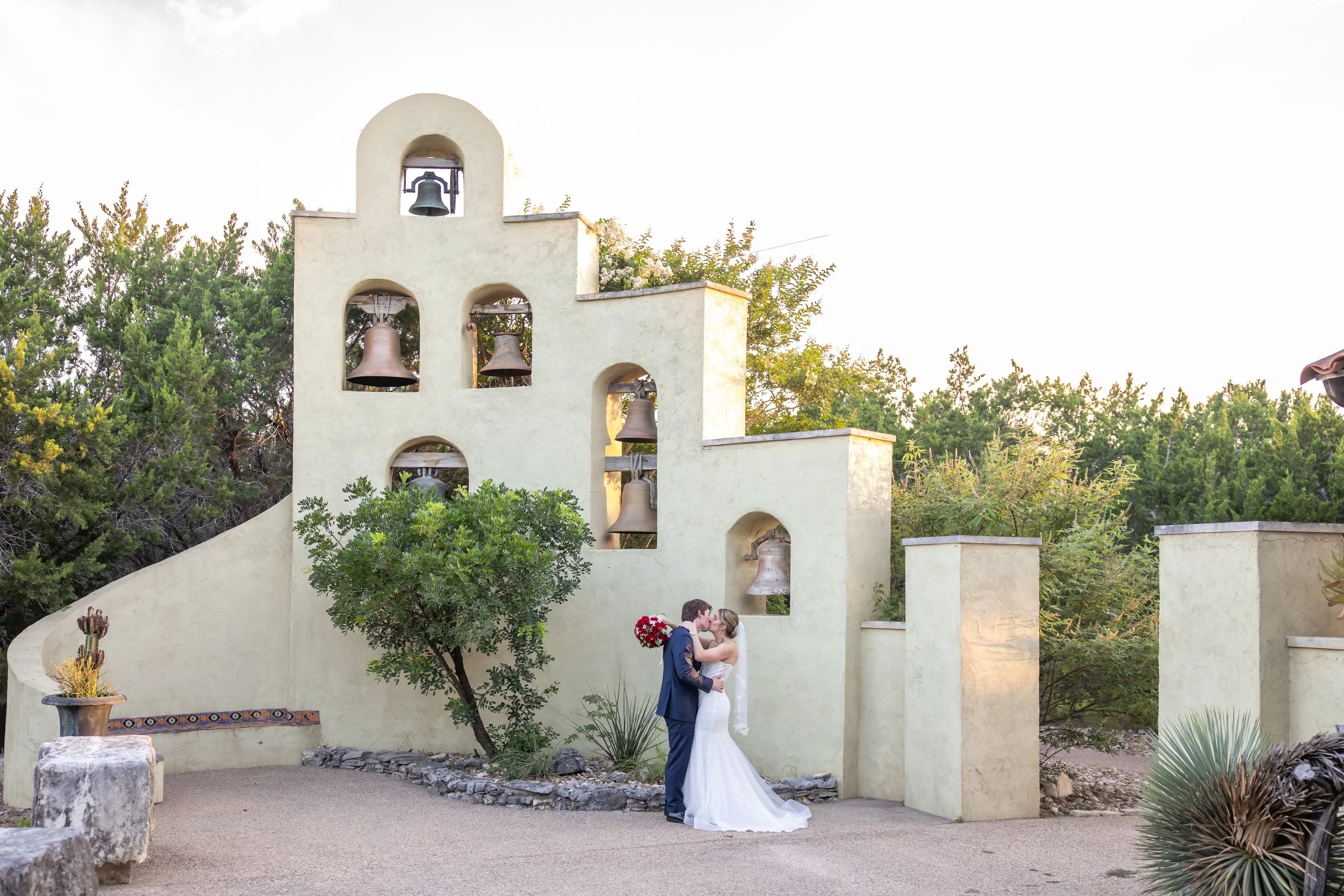 A couple in wedding attire sharing a kiss in front of a bell tower